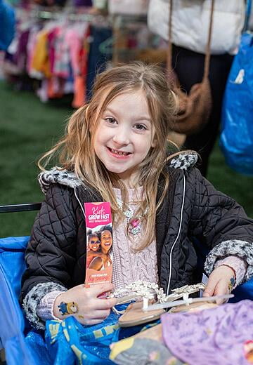 A young girl wearing a winter coat, sitting in a blue wagon, smiles